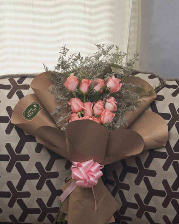 Ramo de 12 rosas rosadas con caspia, estructura en niveles y envoltura de papel kraft, arreglo floral elegante visto de frente.