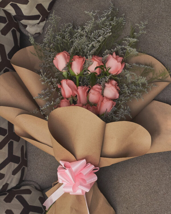 Vista superior de ramo con 12 rosas rosadas y caspia, estructura en niveles, envuelto en papel kraft.