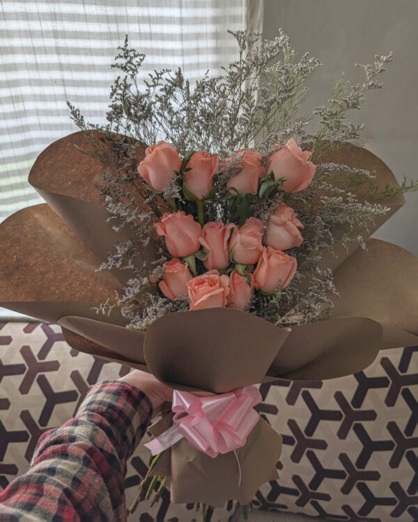 Persona sosteniendo ramo de 12 rosas rosadas con caspia, estructura en niveles y envoltura de papel kraft.
