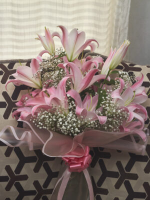 Ramo de lirios orientales acapulco rosas con gypsophila, envuelto en papel coreano rosado transparente y decorado con moño rosado, arreglo floral elegante visto de frente.