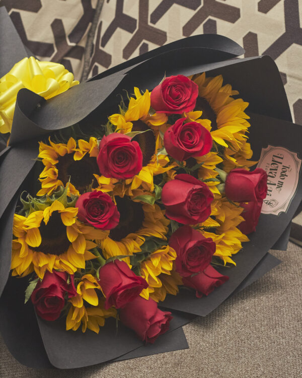 Detalle cercano de girasoles y rosas rojas en ramo con papel negro, mostrando contraste de colores y texturas.