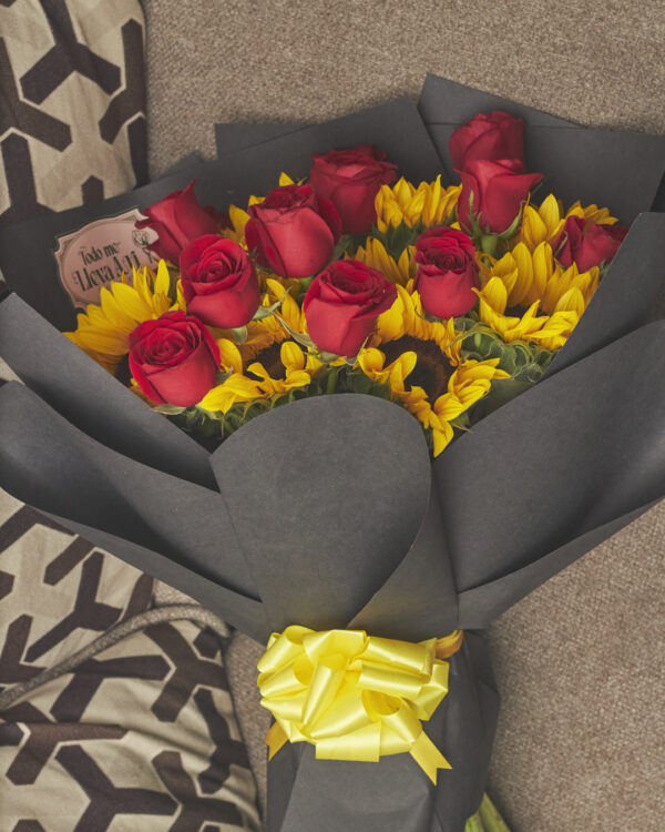 Vista superior de ramo con girasoles y rosas rojas, envuelto en papel negro y con estructura redonda.