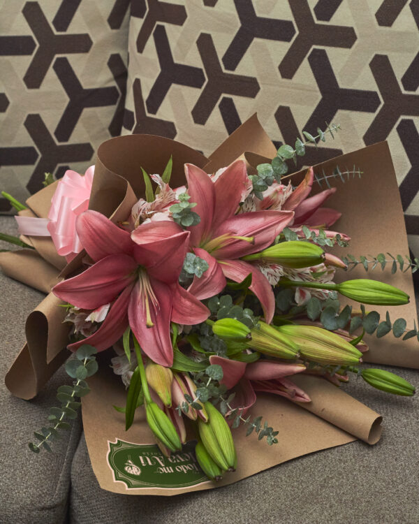ramo_de_lirios_rosas_astromelias_minidolar_2 Detalle cercano de lirios rosas y astromelias con mini dólar en ramo envuelto en papel kraft, mostrando textura y frescura floral.