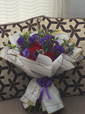 Ramo buchón de rosas rojas con lisianthus morados, envuelto en papel coreano blanco, arreglo floral lujoso visto de frente.