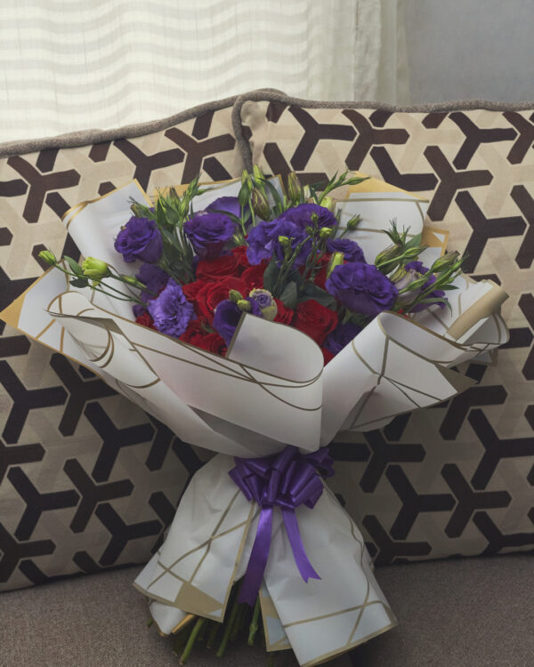 ramo_de_rosas_y_lisianthus_1 Ramo buchón de rosas rojas con lisianthus morados, envuelto en papel coreano blanco, arreglo floral lujoso visto de frente.