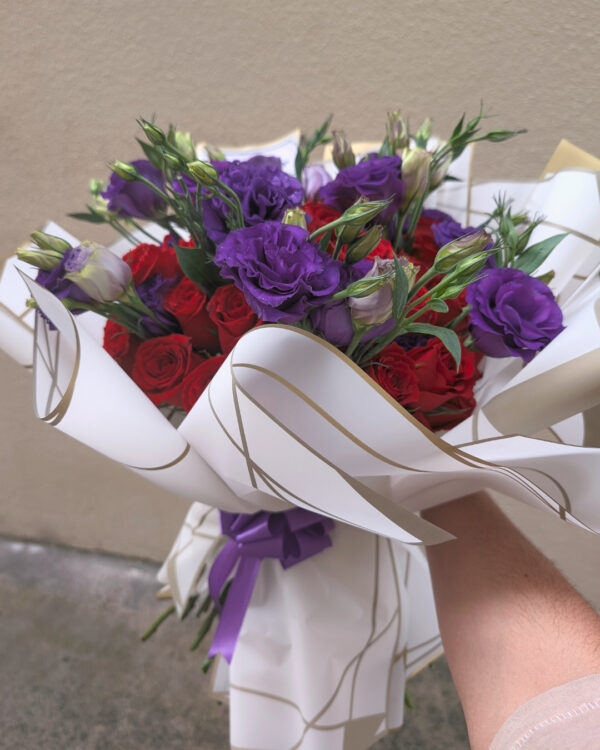 ramo_de_rosas_y_lisianthus_2 Persona sosteniendo ramo buchón de rosas rojas y lisianthus morados envuelto en papel coreano blanco, arreglo floral voluminoso listo para entregar.