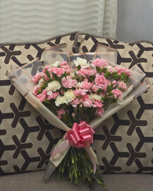 Ramo de claveles en tonos blanco y rosa, envuelto con papel coreano y decorado con moño rosa, arreglo floral delicado visto de frente.