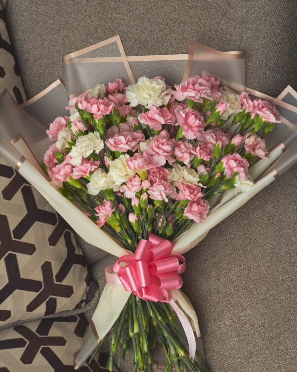 Vista superior de ramo con claveles blancos y rosas, envuelto en papel coreano con moño rosa.