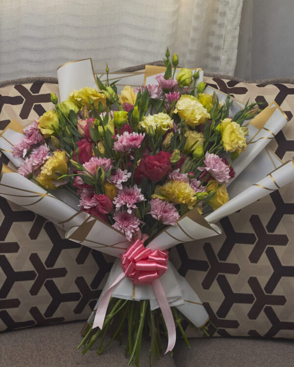 Ramo de lisianthus amarillo y vino con crisantemos lilas malibú, envuelto en papel coreano blanco y decorado con moño rosado, arreglo floral equilibrado visto de frente.