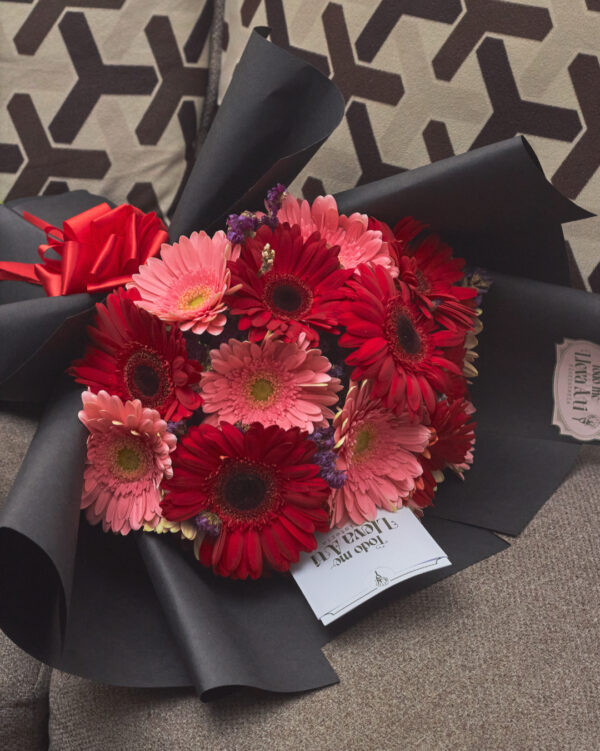 ramo_de_gerberas_bicolor_con_statice_3 Detalle cercano de gerberas bicolor y flor statice en ramo redondo con envoltura negra, mostrando textura y contraste floral.