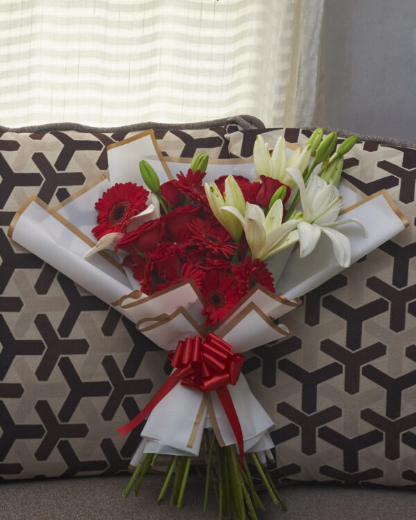 Ramo de gerberas, rosas rojas y lirios blancos con envoltura de papel coreano blanco, arreglo floral de estructura coreana visto de frente.
