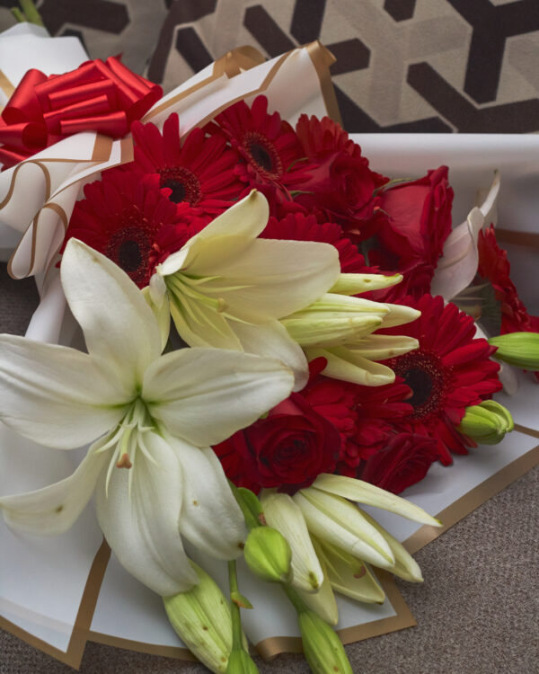 Detalle cercano de flores rojas y lirios blancos en ramo con papel coreano blanco, mostrando textura y contraste del arreglo coreano.