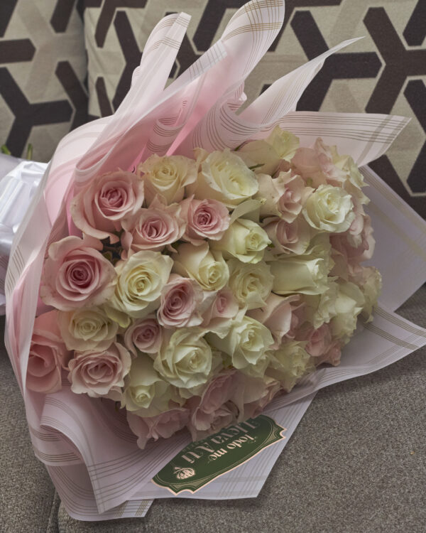 ramo_buchon_de_rosas_tonos_pastel_5 Detalle cercano de rosas en tonos pastel rosados y blancos en ramo envuelto en papel coreano rosa con moño blanco, mostrando textura y suavidad floral.